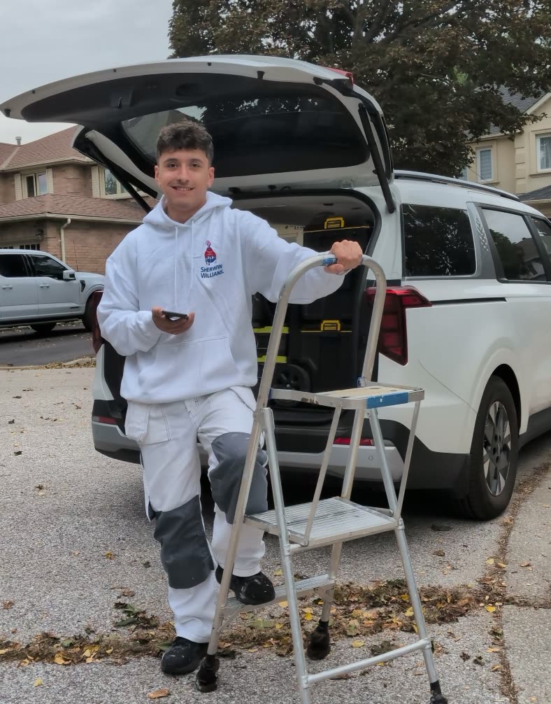 Dylan, the owner of Prep Prime Paint, in painter's whites beside his work van and step ladder.